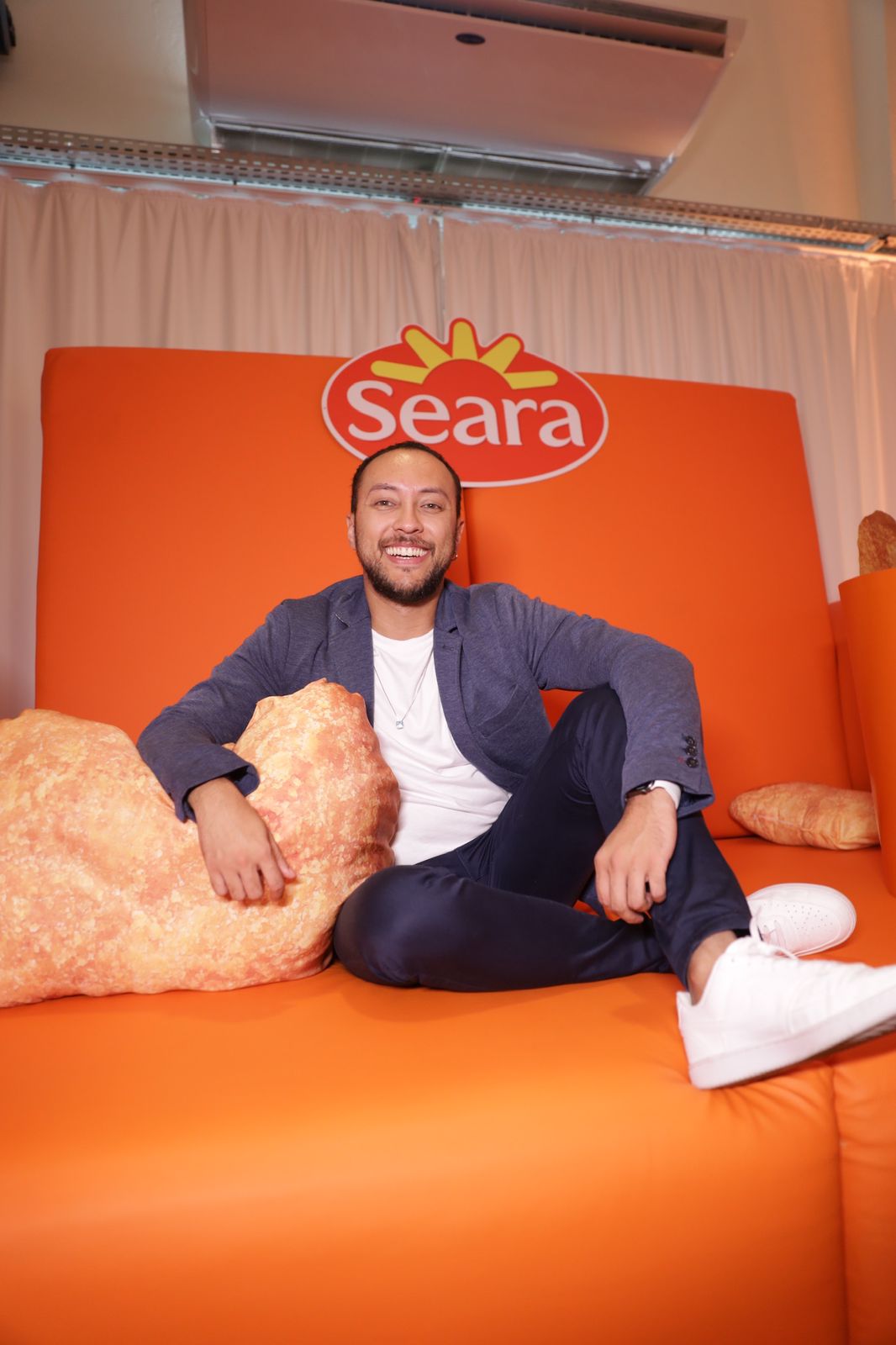 Anselmo Penha em sofá laranja com o logo da Seara
